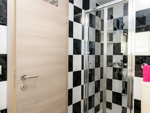 Un baño con pared de baldosas blancas y negras en damero, cabina de ducha de vidrio y puerta de madera con cerradura.