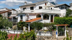 A white villa with a red-tiled roof, multiple balconies, and a stone wall entrance. - Lovely Apartment With Terrace & Garden Grill (Malinska-Dubasnica)