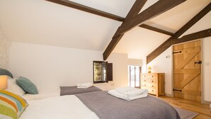 A bedroom with a large bed, two smaller beds, wooden beams, a wooden wardrobe, and a sliding barn-style door. - Holiday Home in Tavistock With Garden (Tavistock)