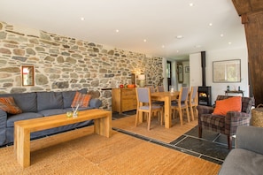 A cozy living room with a stone wall, a fireplace, and a dining area with wooden furniture. - Holiday Home in Tavistock With Garden (Tavistock)