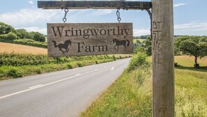 A wooden sign reading "Wringworthy Farm" with two horse silhouettes, mounted on a wooden post beside a rural road. - Holiday Home in Tavistock With Garden (Tavistock)