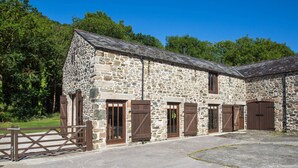 A stone building with multiple doors and windows, surrounded by a paved area and greenery. - Holiday Home in Tavistock With Garden (Tavistock)