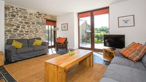 A living room with a stone wall, a grey sofa, a wooden coffee table, and a television on a stand. - Holiday Home in Tavistock With Garden (Tavistock)