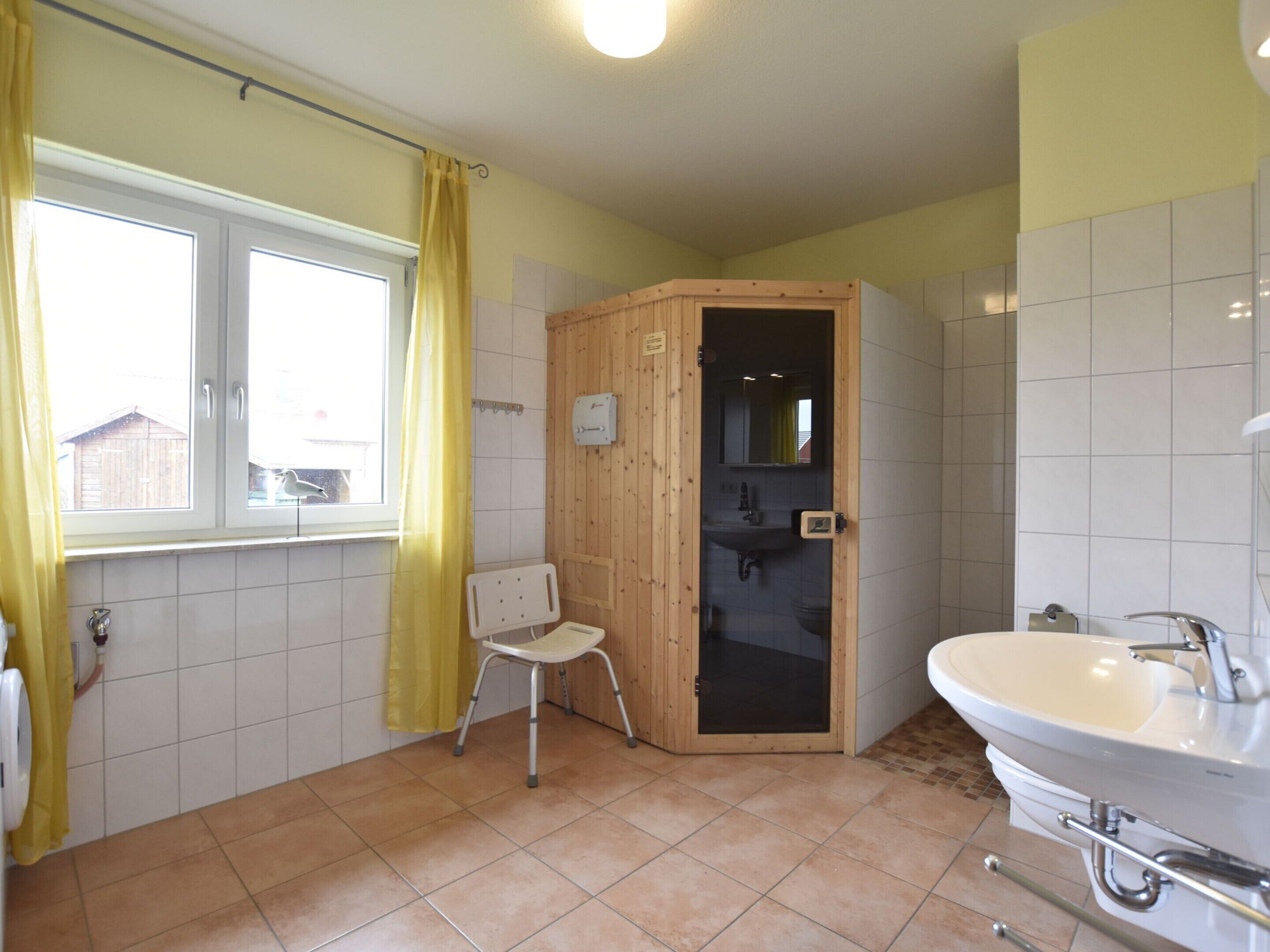 A bathroom with a wooden shower enclosure, a white sink, and a window with yellow curtains.