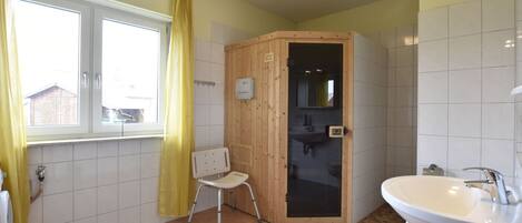 A bathroom with a wooden shower enclosure, a white sink, and a window with yellow curtains.