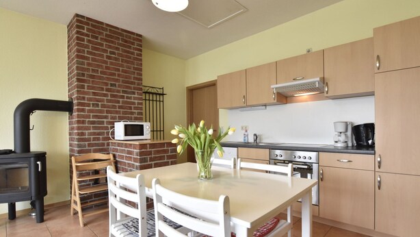 A kitchen with a brick fireplace, a microwave, and a stove. There is a dining table with chairs and a vase of flowers. - Ferienwohnung in Zierow Nahe Meeresstrand (Zierow)