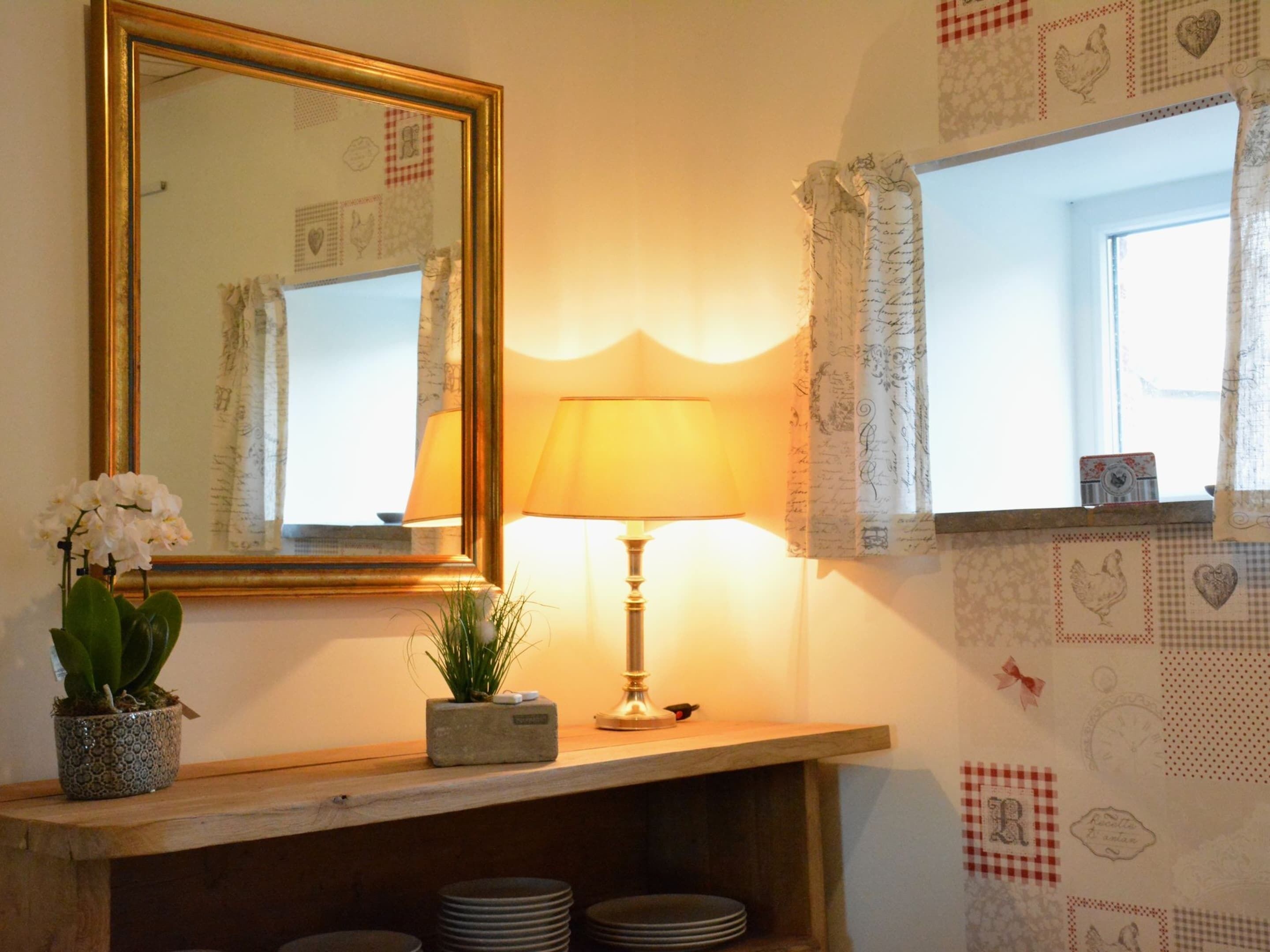 A room with a wooden shelf holding a lamp, a potted plant, and a framed mirror.