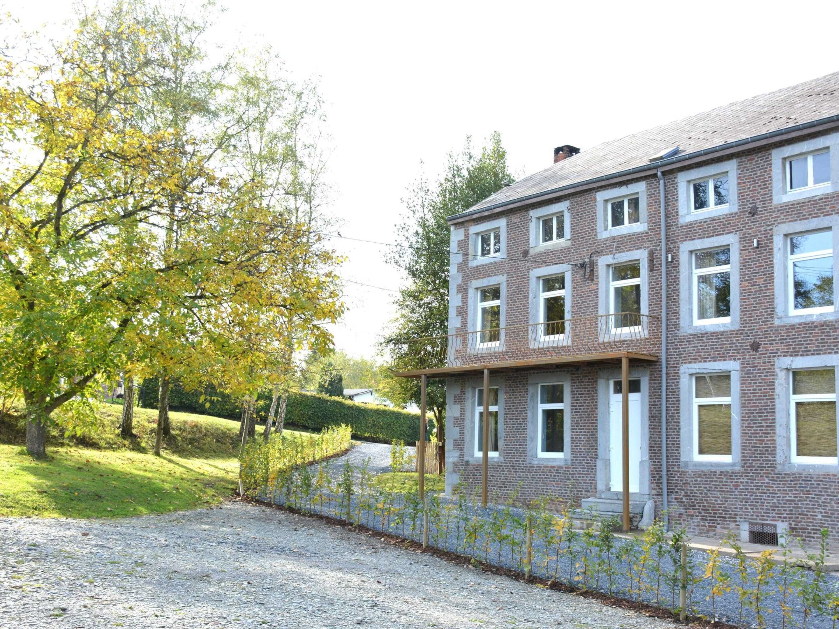 A multi-story brick building with a gravel driveway and a hedge.