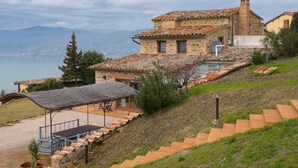 A stone house with a tiled roof, a swimming pool, and a view of a lake. - Villa in Cortona With Private Pool (Magione)