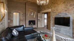 A cozy living room with a fireplace, leather sofa, and a modern chandelier. - Villa in Cortona With Private Pool (Magione)