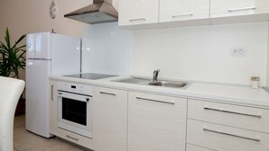 Una cocina moderna con armarios blancos, un lavamanos de acero inoxidable, horno empotrado y campana extractora.