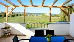 Un patio cubierto con una mesa y sillas, vistas a un paisaje verde y agua, y una barandilla de metal.