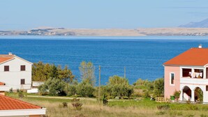 Vista costera con mar azul cristalino, un edificio blanco de techo rojo y un edificio rosa con balcón.