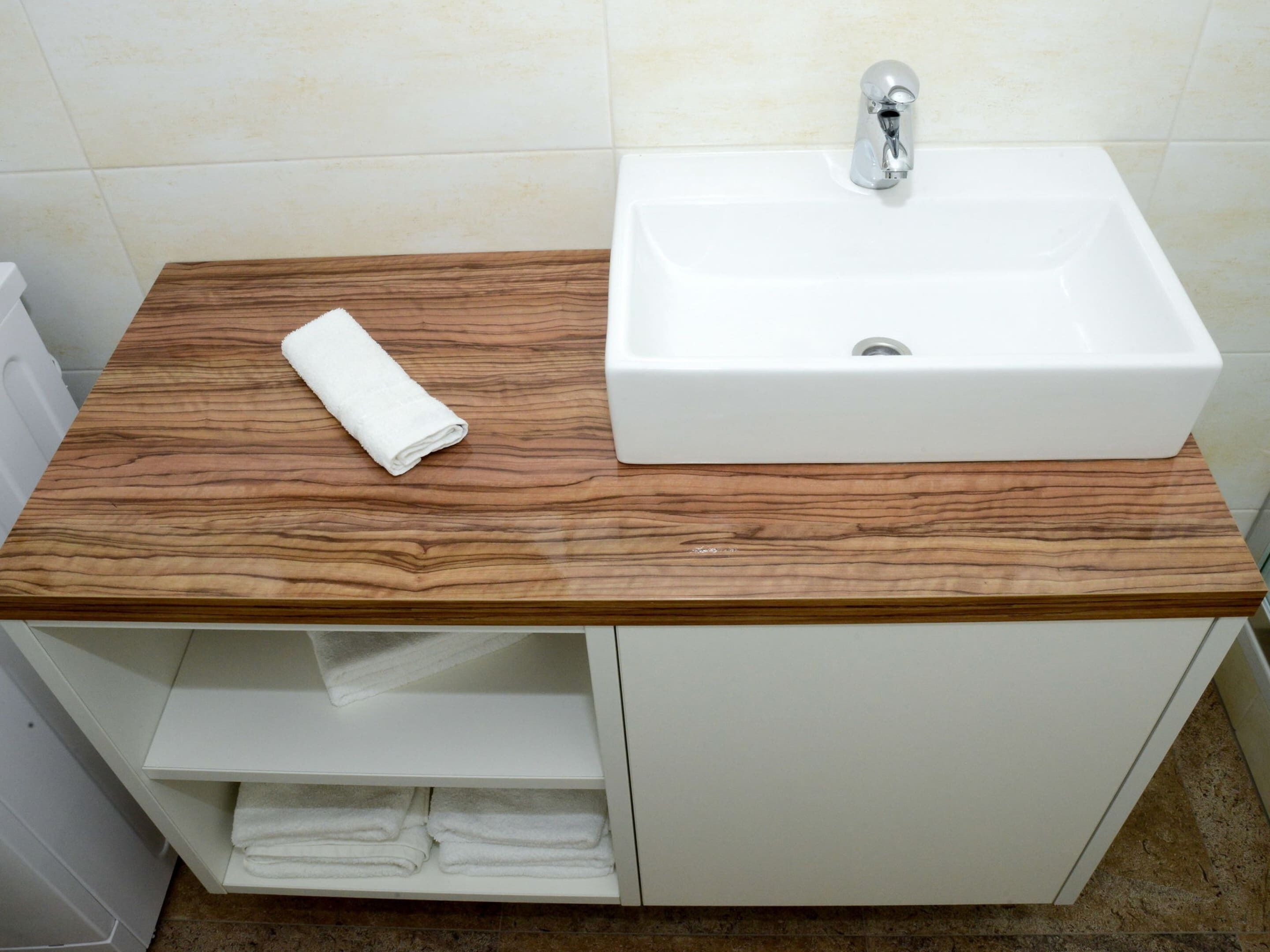 Ein Badezimmer mit einem weißen Waschbecken, einer Holzauslage und einem Handtuch auf der Auslage.
