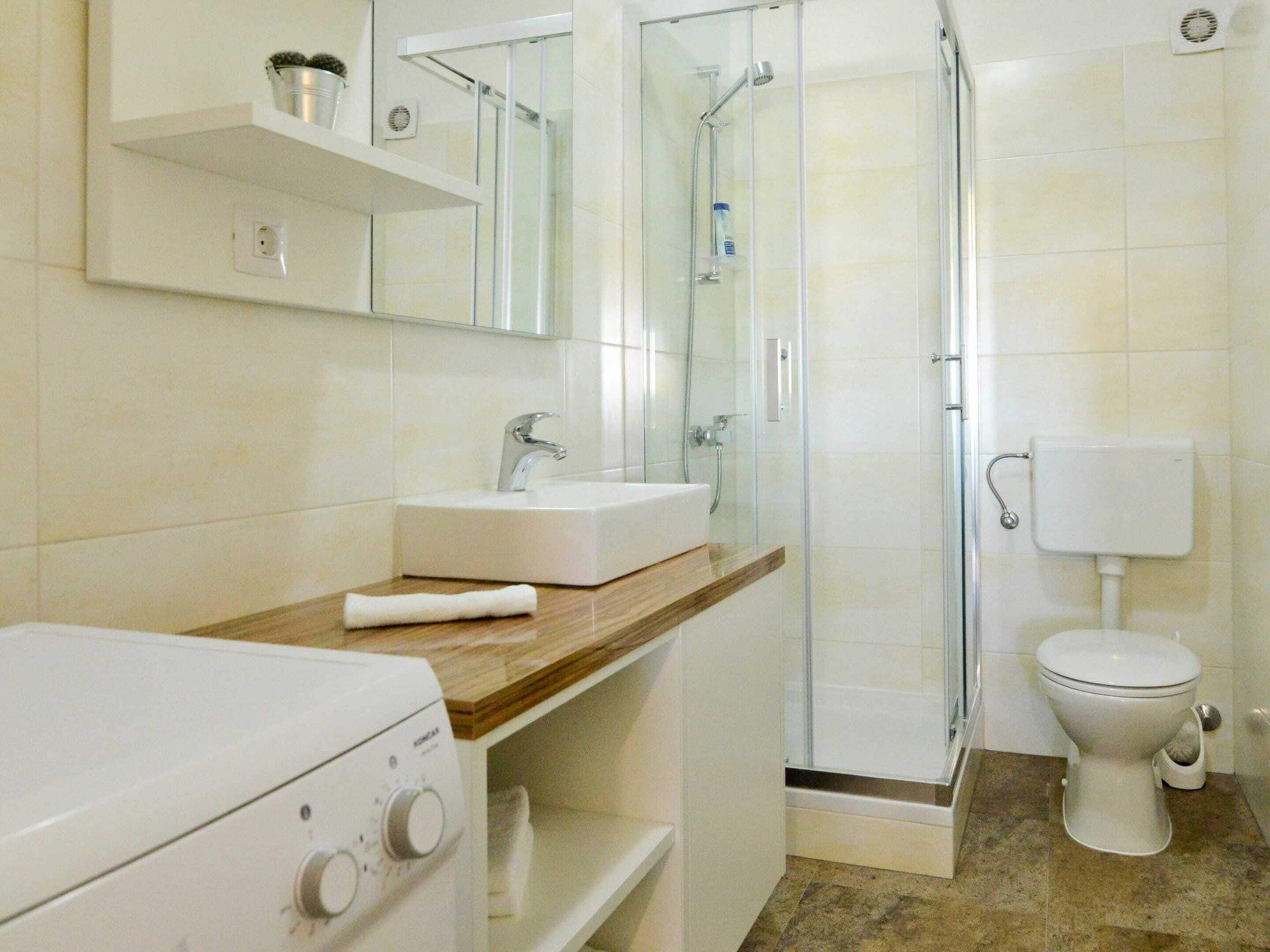 Ein Badezimmer mit weißem Waschbecken, einem Spiegel darüber, einer Duschkabine und einer Toilette.