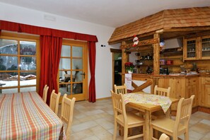 A dining area with a table and chairs, a kitchen with wooden cabinets, and a window with red curtains. - Accommodation With Wellness Center, in Val di Sole (Caldes)