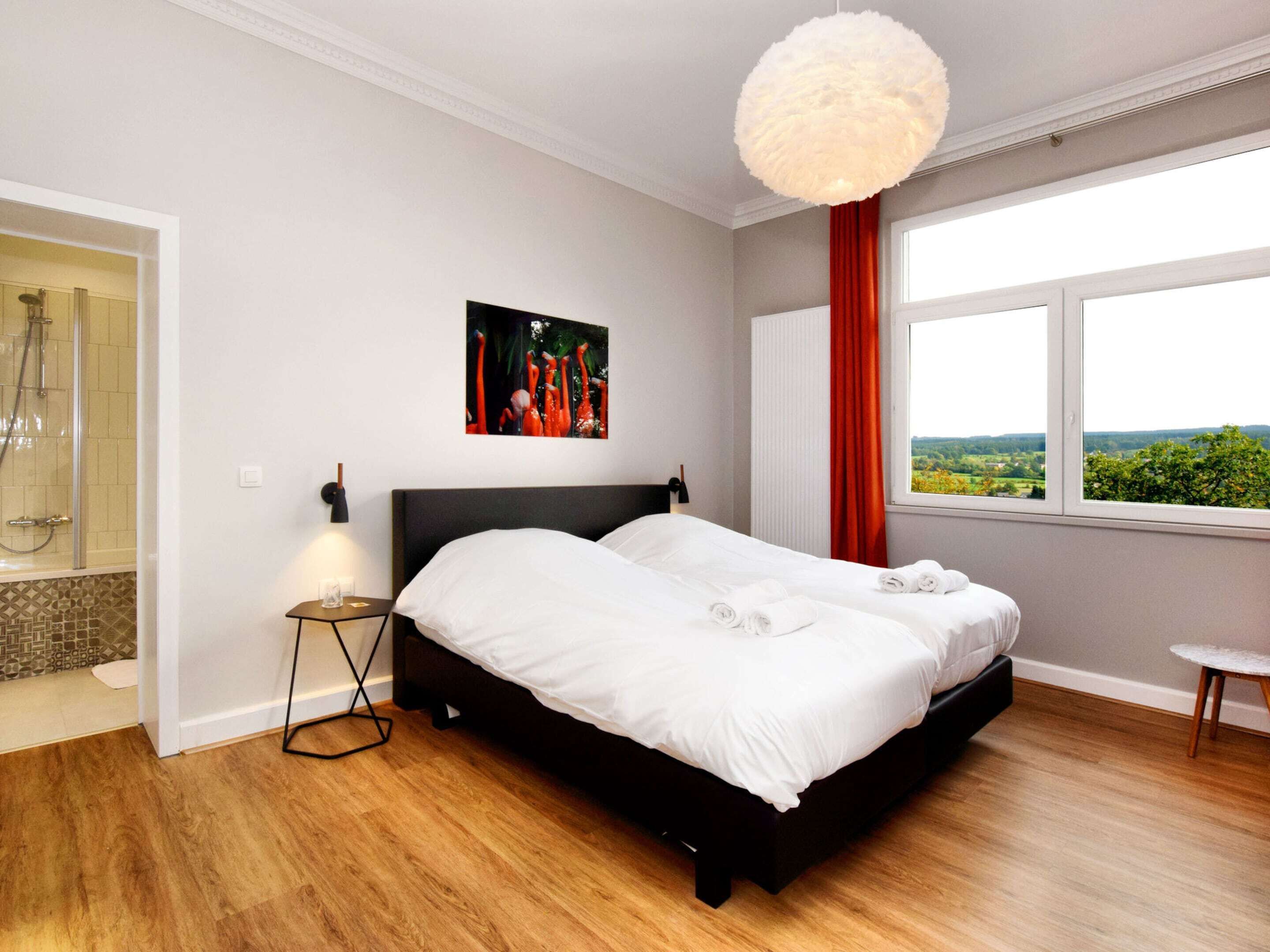 A modern bedroom with a large bed, a view of the outdoors, and a shower area.