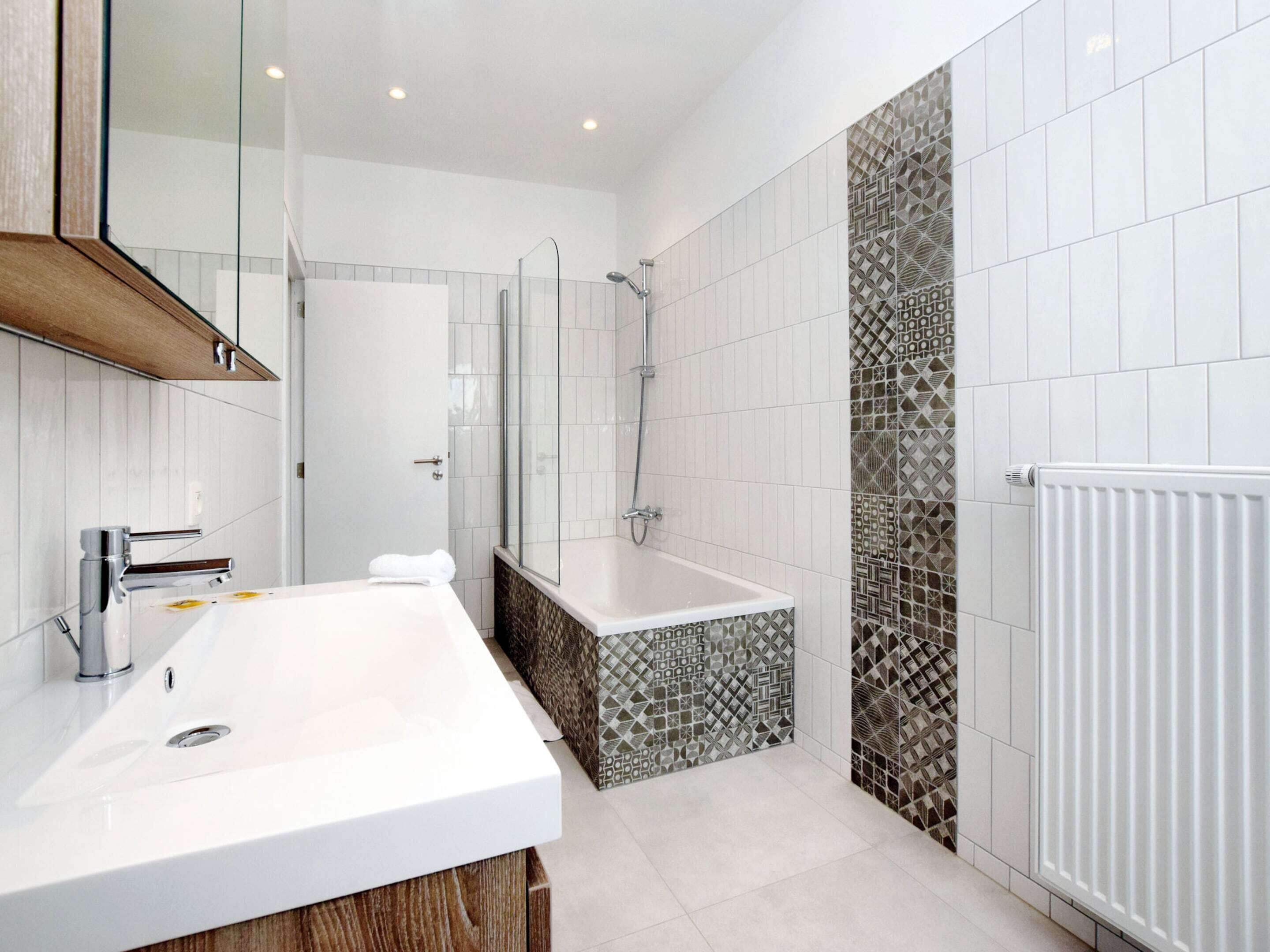 A modern bathroom with a large white sink, a glass shower enclosure, and patterned tiles on the walls.