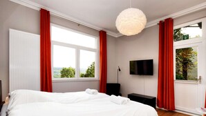 A bedroom with a large bed, a flat-screen TV, a desk, and a window with red curtains. - Affluent Holiday Home in Spa with Hot Tub, Garden, Sauna (Spa)