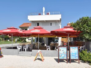An outdoor seating area with red umbrellas, a signboard, and a building in the background. - Modern Apartment in Pakostane With Barbecue (Pakostane)