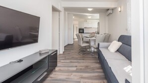 A modern living room with a flat-screen TV, a sofa, and a dining area in the background. - Modern Apartment in Pakostane With Barbecue (Pakostane)