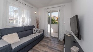 A modern living room with a grey sofa, a flat-screen TV, and a sliding glass door leading to a balcony. - Modern Apartment in Pakostane With Barbecue (Pakostane)