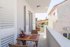 A balcony with a wooden table, chairs, a bowl of fruit, and a bottle of champagne. - Modern Apartment in Pakostane With Barbecue (Pakostane)