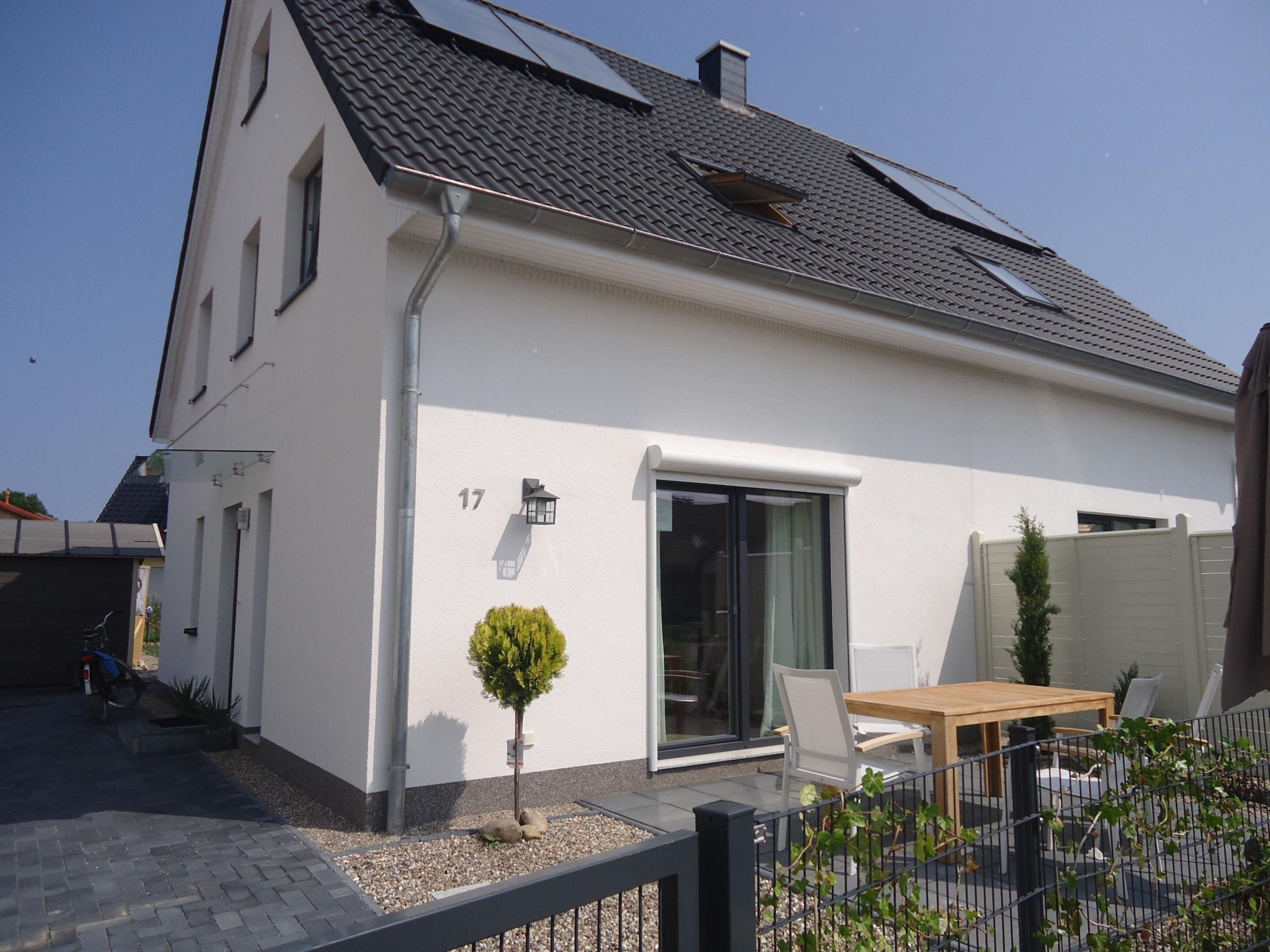A modern house with a tiled roof, a small garden, and a patio with outdoor furniture.