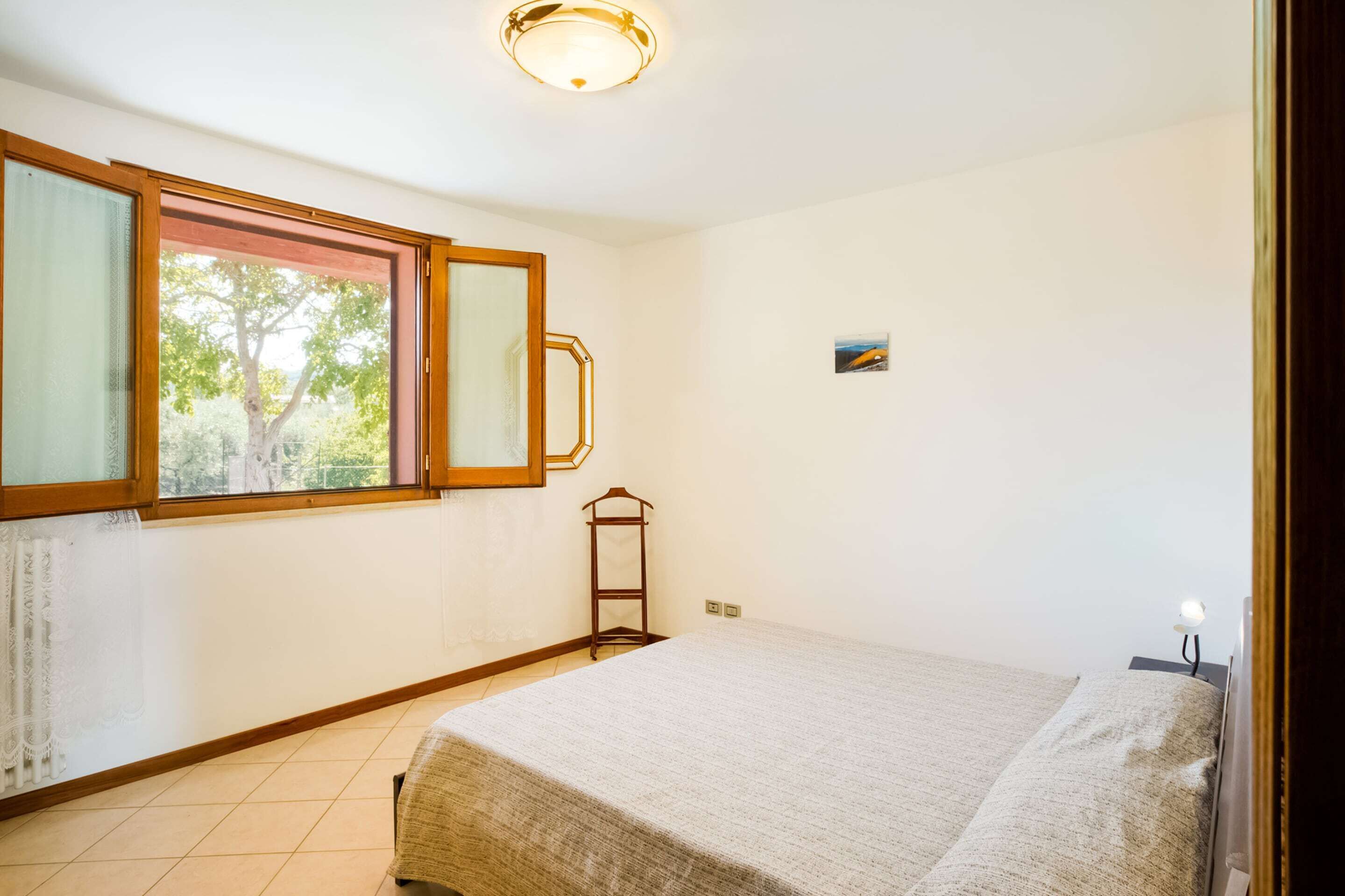 A room with a bed, a window with a view of trees, a small table, and a wall-mounted picture.