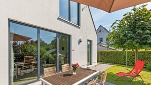 Une terrasse avec une table et des chaises, une porte vitrée et une chaise rouge, le tout dans un cadre de jardin.