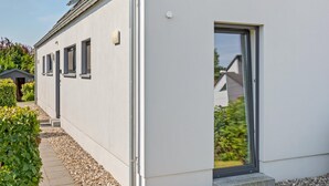 Un bâtiment moderne à l’extérieur blanc, doté d’une allée couverte et d’une porte donnant sur un jardin.