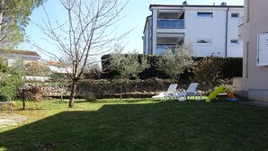 A grassy yard with white lounge chairs and a yellow slide. - Large Apartment in Malinska near Sea (Malinska-Dubasnica)