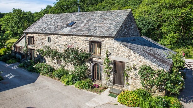 A stone house with a sloped roof, a small porch, and a garden with various plants and flowers.