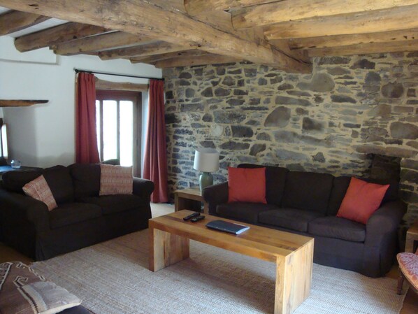 A cozy living room with two dark sofas, a wooden coffee table, and a stone wall. - Holiday Home in Tavistock With Garden BBQ (Tavistock)