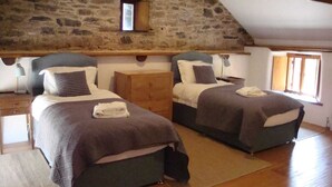 A room with two beds, wooden floors, stone walls, a small window, and a wooden dresser.
