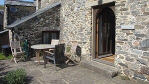 A stone cottage with a small patio, a round table, and two chairs.