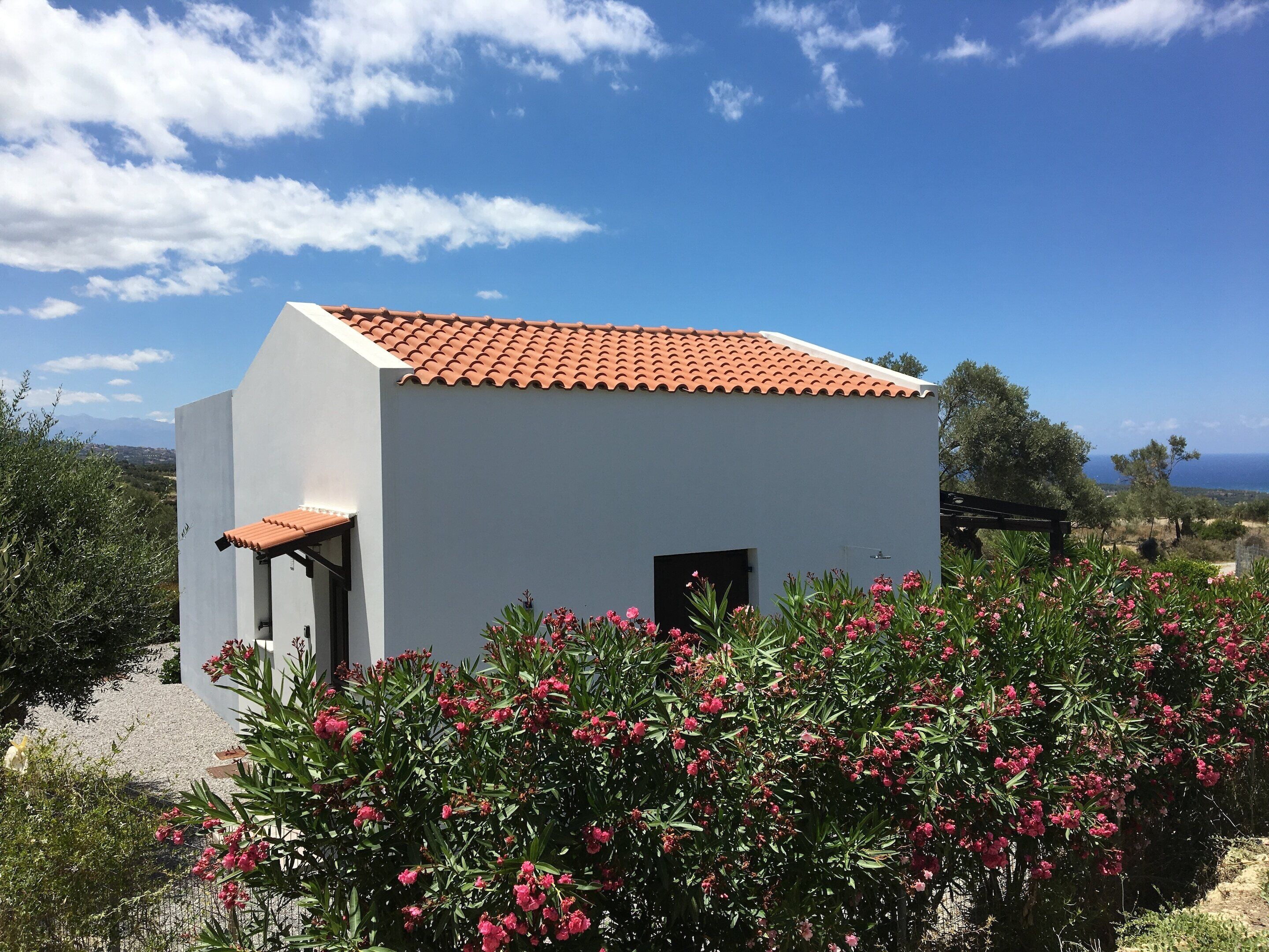 A small white building with a red-tiled roof, surrounded by greenery and a clear sky.