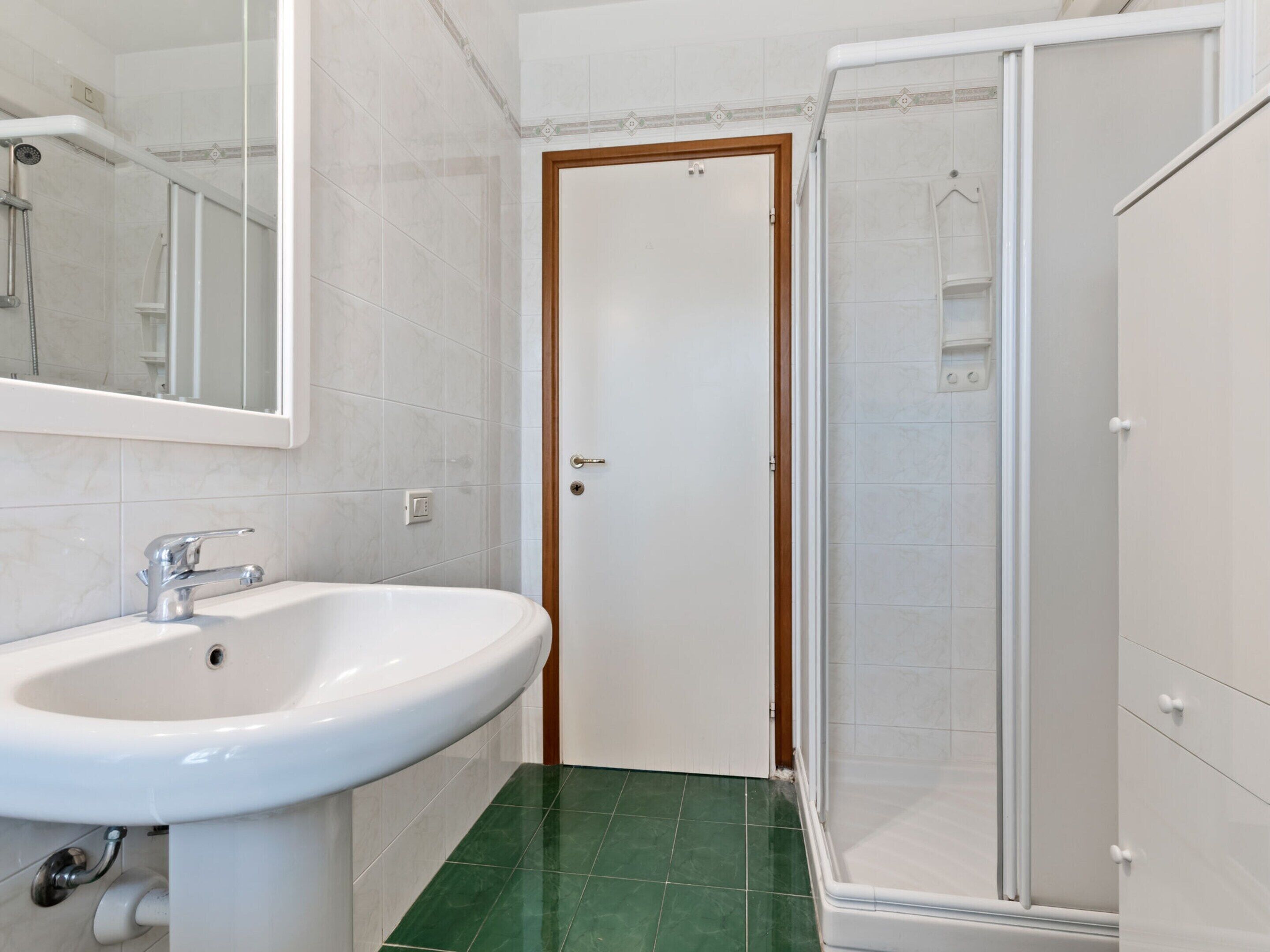 A bathroom with a white sink, a mirror, a shower enclosure, and a door.