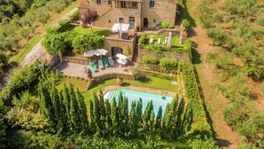 Uma vila de pedra com piscina, rodeada por vegetação exuberante e um caminho sinuoso.