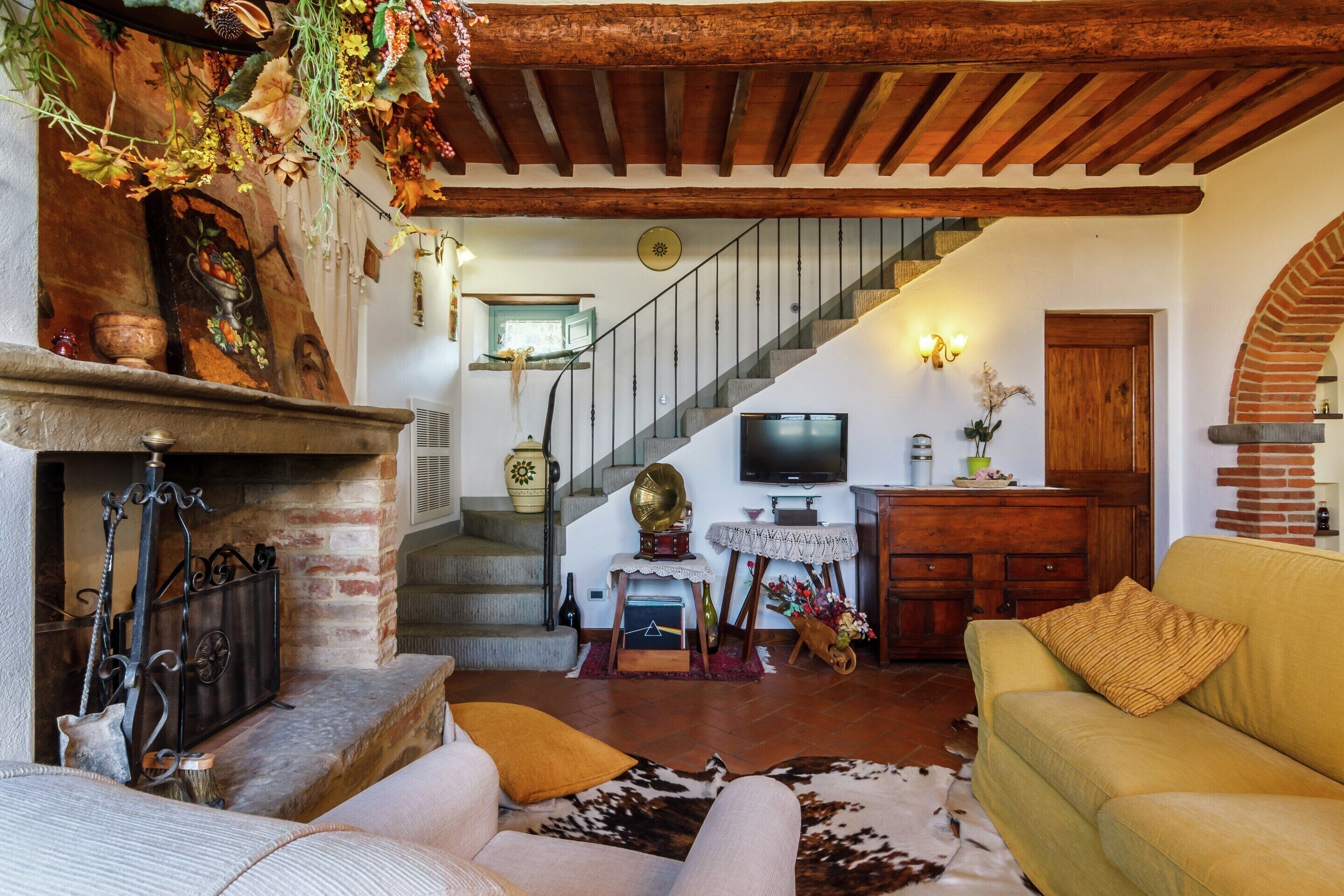 A rustic living room with a fireplace, a staircase, a television, and a sofa.