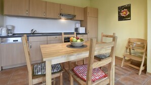 A compact kitchen with wooden cabinets, a dining table with chairs, and a fruit bowl. - Ferienwohnung in Zierow (Zierow)