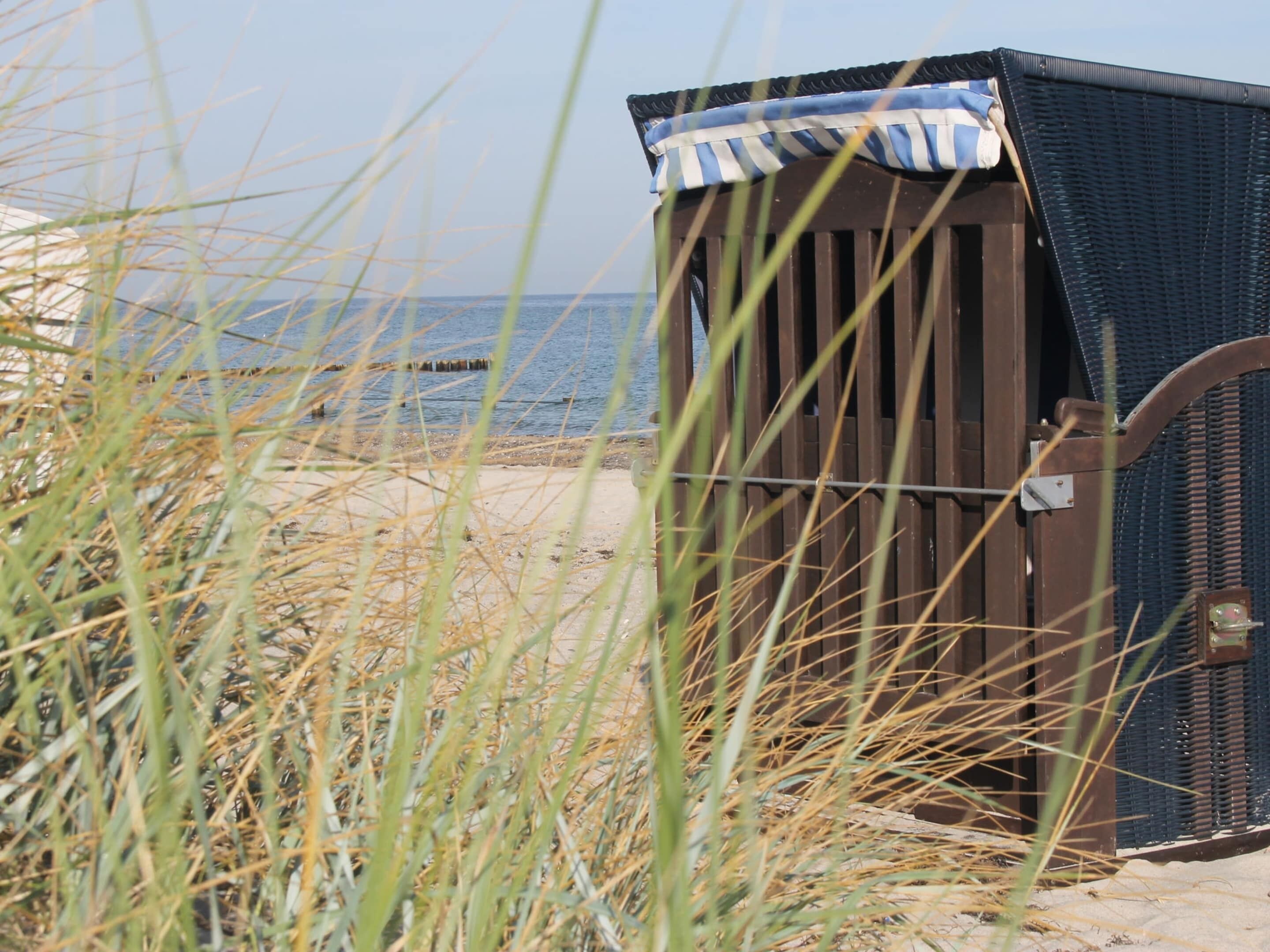 Een strandhut met een gestreepte luifel, gelegen op een zandstrand met gras op de voorgrond.