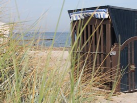 Una cabaña playera con toldo a rayas, ubicada en una playa arenosa con césped al frente.