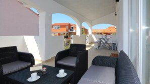 Un espacio al aire libre cubierto con muebles de mimbre, una mesa y vista a edificios al fondo.