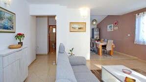 Una sala moderna con un sofá gris, un comedor con mesa y sillas, y una cocina con refrigerador.