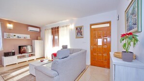 Una sala moderna con un sofá gris, un televisor, una estantería y una puerta.