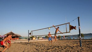 Partido de voleibol de playa con jugadores en bañadores, una red y una cancha de arena.