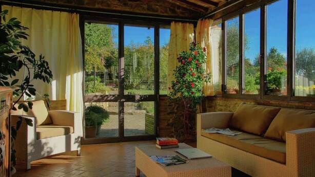 A cozy room with wicker furniture, a coffee table, and large windows offering a view of a garden. - Belvilla by OYO Villa Sara (Lucignano)