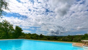 A clear blue swimming pool surrounded by greenery and a cloudy sky. - Belvilla by OYO Villa Sara (Lucignano)