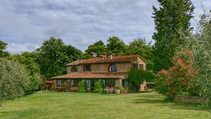 A stone house with a tiled roof, surrounded by a grassy lawn and trees. - Belvilla by OYO Villa Sara (Lucignano)